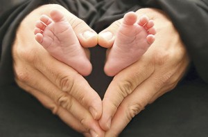This is a photo of a dad with his hands in a heart shape holding his 3 week old infants feet.